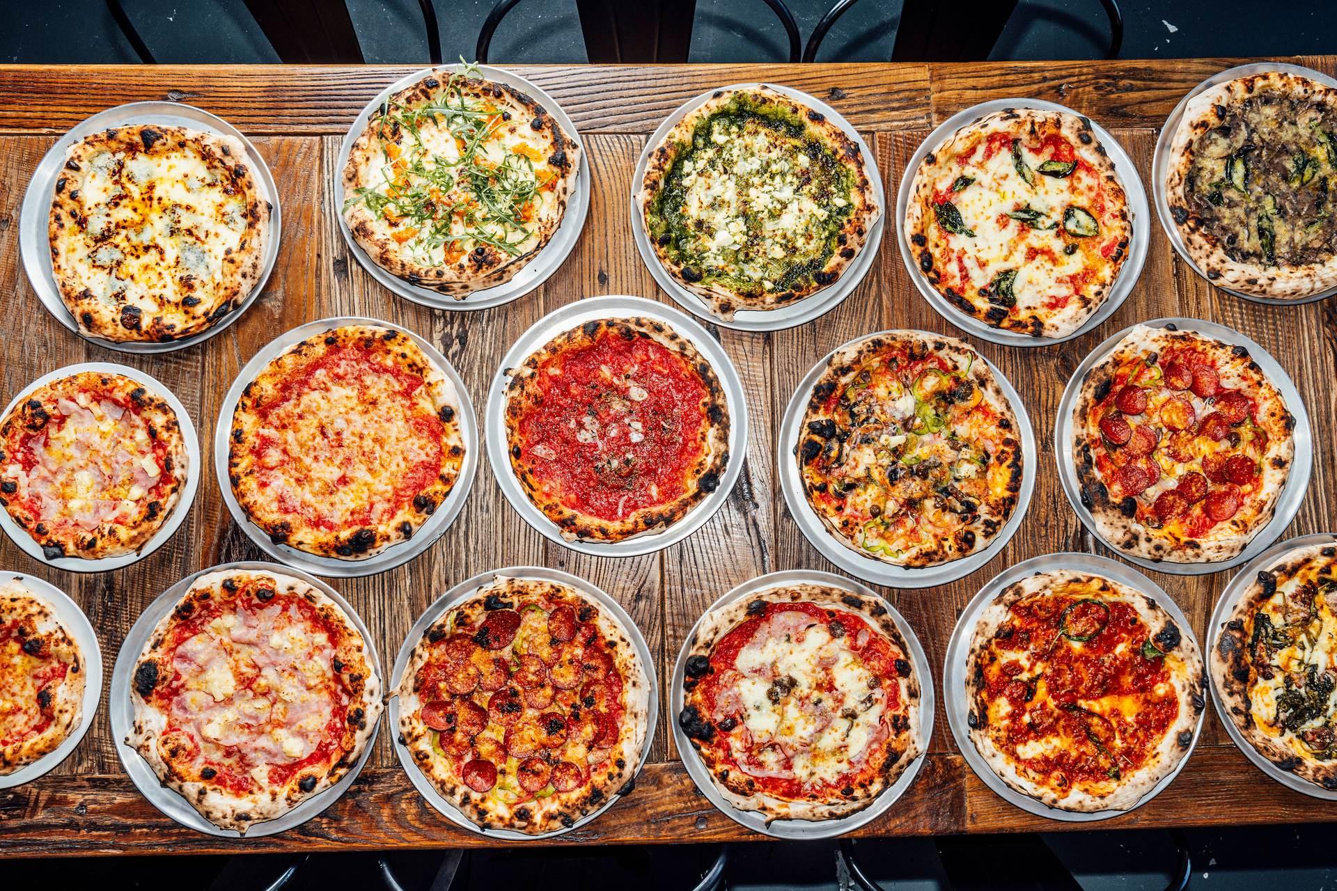 Eighteen wood-fired pizzas laid out on a long timber table at Tillage Pizza